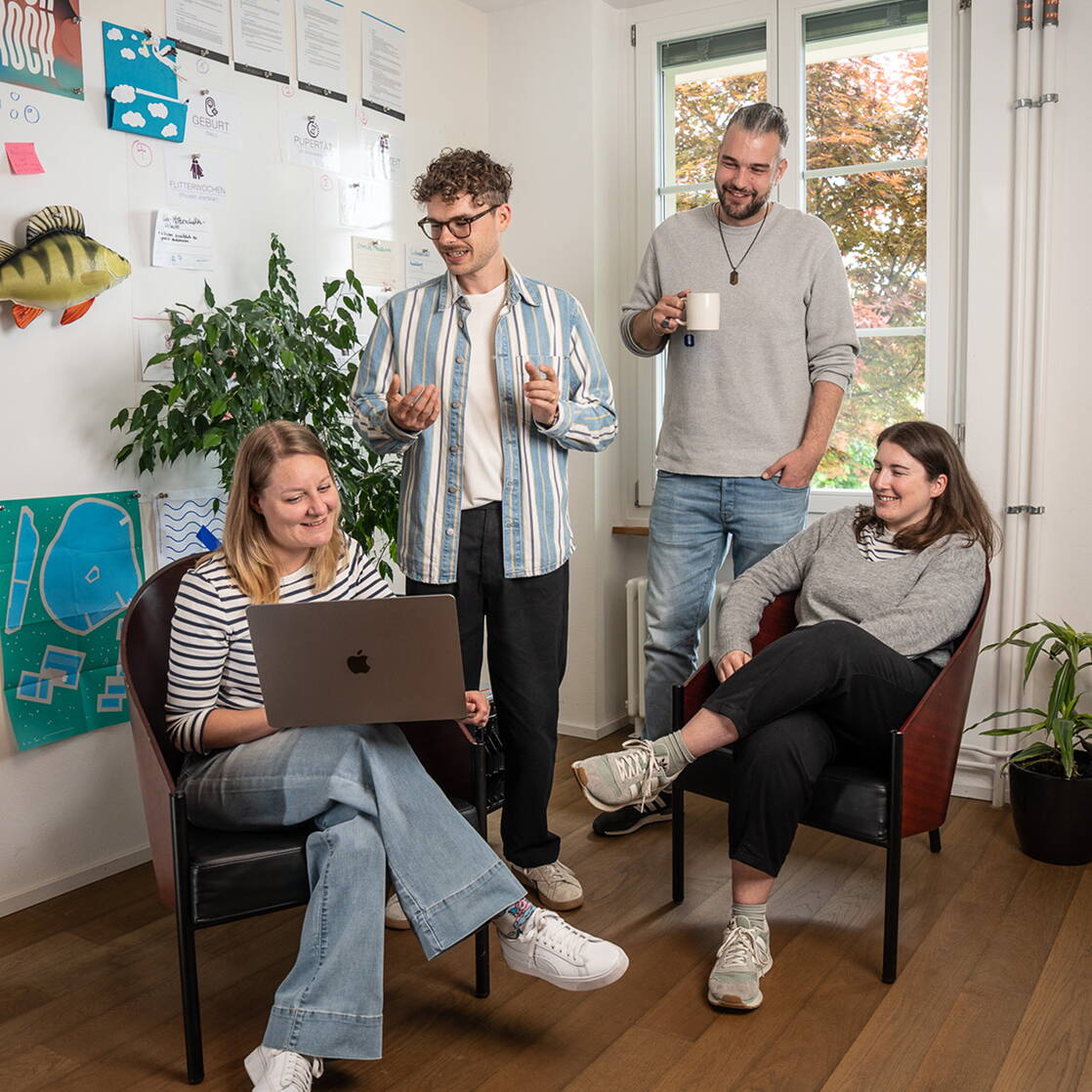 Team von cmsbox Austausch in einem hellen Büro mit Laptop, Whiteboard und lockerer Arbeitsatmosphäre.