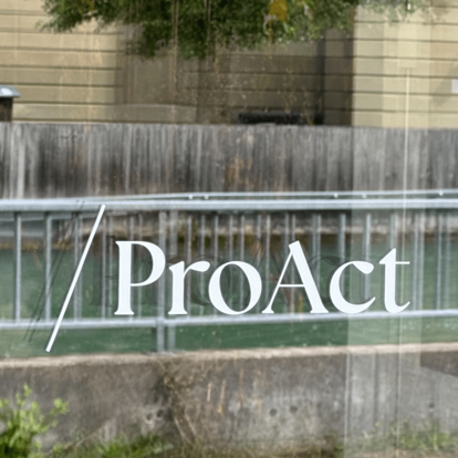 Proact Signaletik Proact Schriftzug an der Glasfassde, in der Spiegelung die Aare