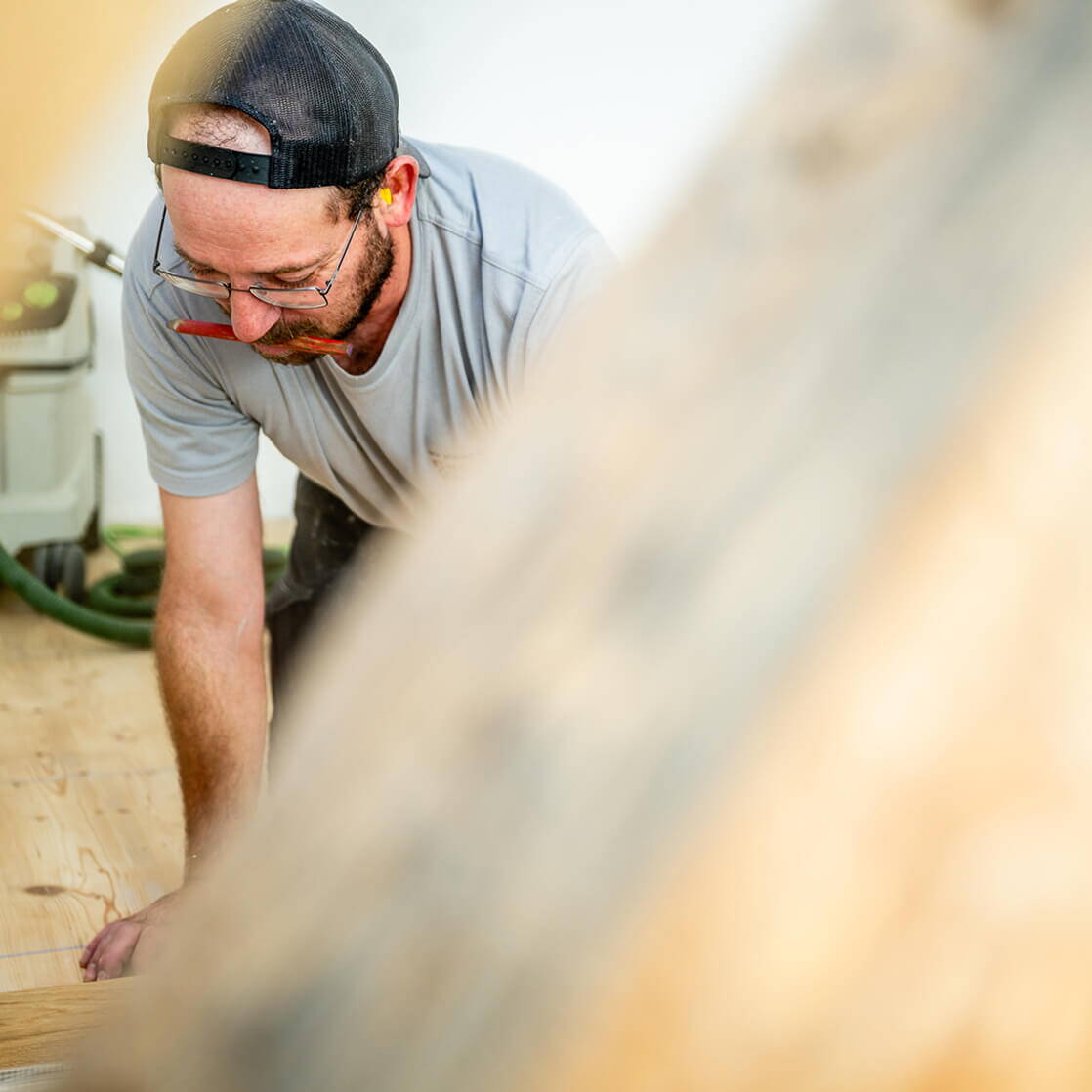 Mitarbeiter bei Holzarbeiten in Innenräumen, mit Bleistift im Mund und unscharfem Holz im Vordergrund.